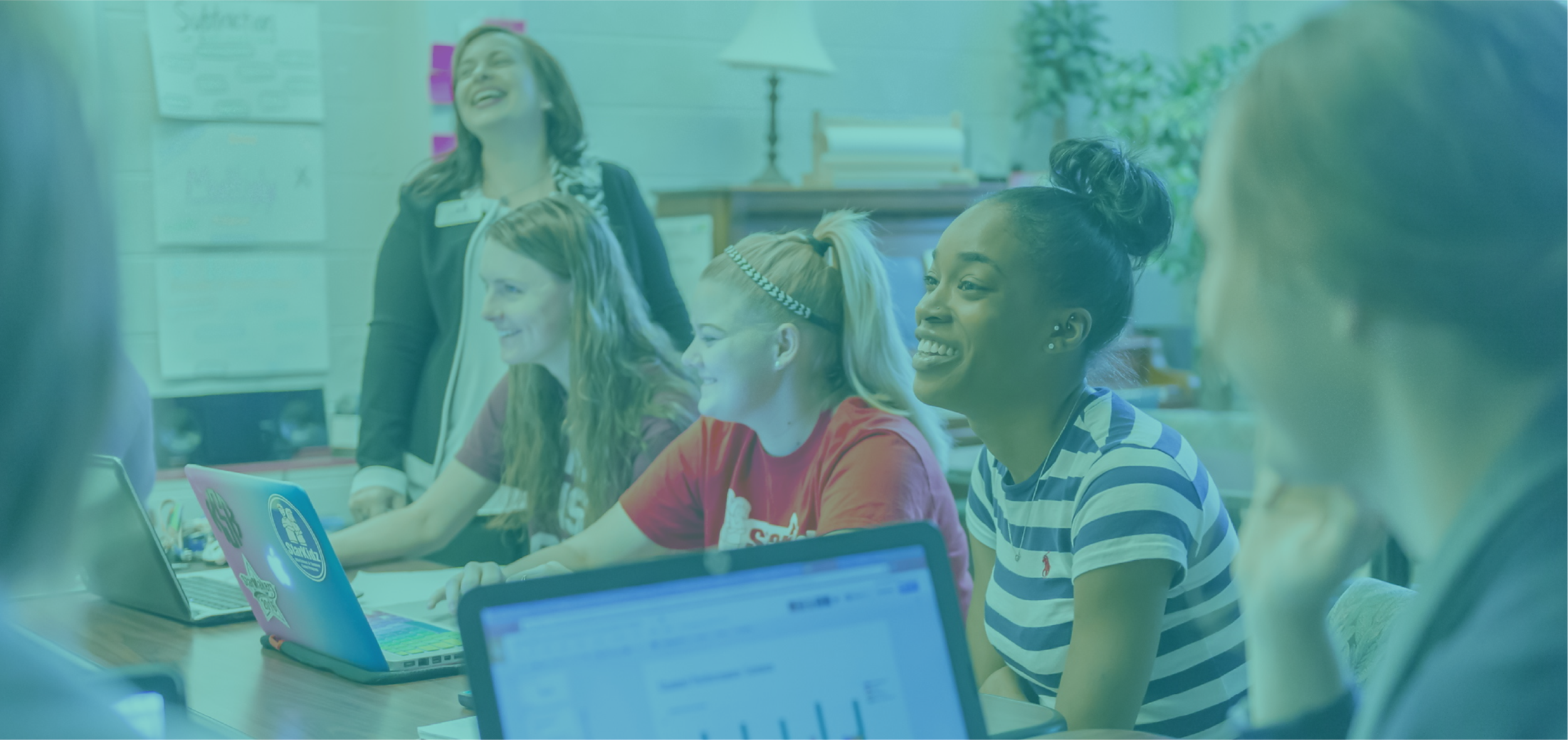 Group of students laughing in classroom setting with teacher.