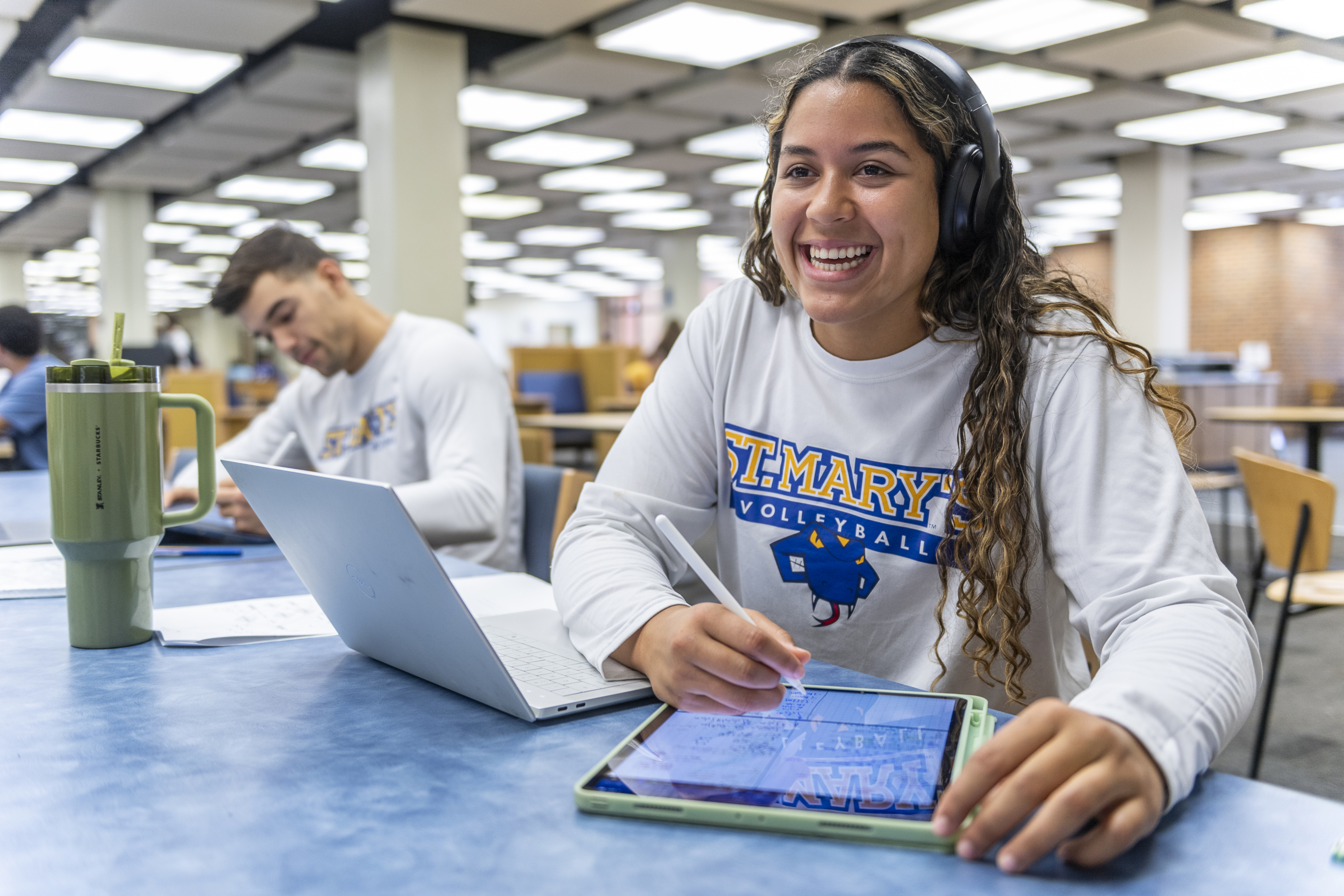 Student with laptop and iPad smiling to the camera.